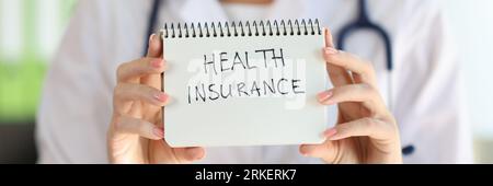 Female doctor shows notepad with words health insurance close up. Stock Photo