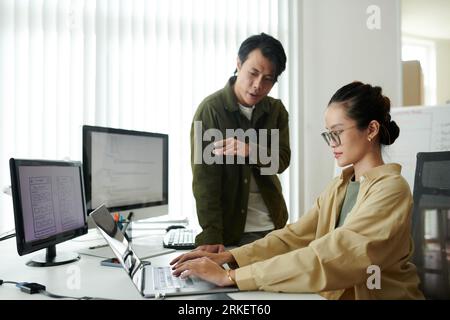 Team leader giving junior developer advice on how to write better programming cod Stock Photo