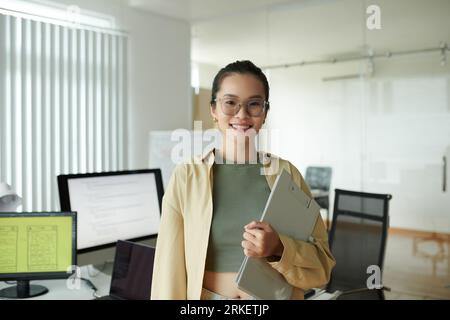 Portrait of positive IT company employee with clipboard standing in office Stock Photo