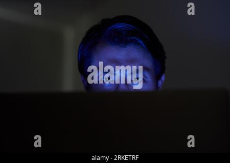 Frowning hacker trying to break into computer system late at night Stock Photo