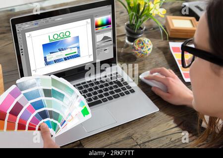 A Woman Holding Color Swatches Using A Laptop With Logo Design Software On The Screen Stock Photo