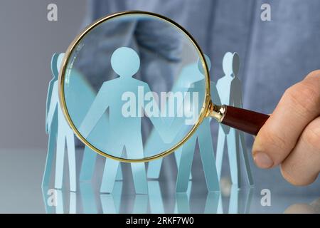 Holding Magnifying Glass And Paper People. Closeup Shot Stock Photo