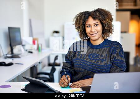 Portrait of confident businesswoman with curly hair writing on adhesive notes in office Stock Photo
