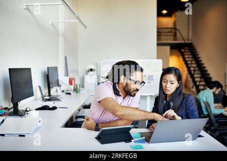 Confident businessman explaining to businesswoman over laptop computer on desk in office Stock Photo