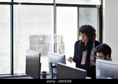 Businesswoman using mobile phone while standing by male colleague in office Stock Photo