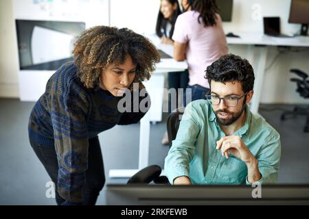 High angle view of confident businessman explaining to businesswoman over desktop computer in office Stock Photo