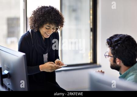 High angle view of smiling businesswoman using mobile phone while talking to male colleague in office Stock Photo