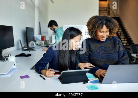 Smiling female colleagues using laptop computer on desk while sitting in office Stock Photo