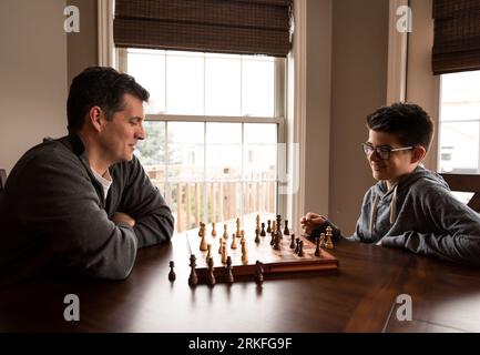 Father and son laughing while playing chess together at the table. Stock Photo
