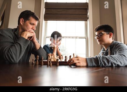 Father and son playing chess at a table while little brother watches. Stock Photo