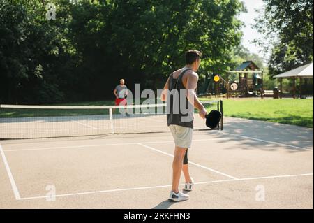 Two young adults playing a game of pickleball near a playground Stock Photo