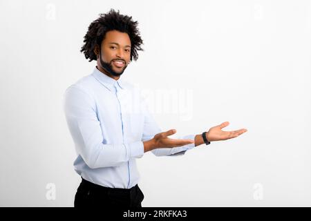 Advertising concept. Handsome curly young man in white shirt presenting, pointing hands aside, advertising new product isolated on white Stock Photo