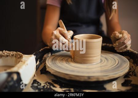 Close up of girl's hands molds clay pot spinning on pottery whee Stock Photo