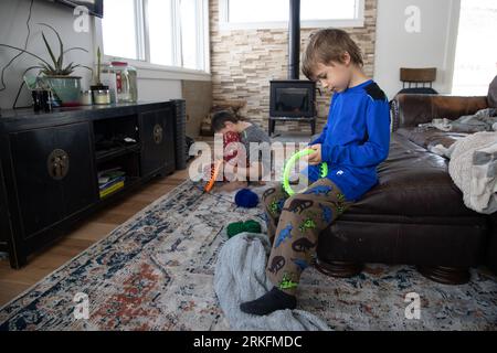 Little boys learning how to loom knit in their living room Stock Photo