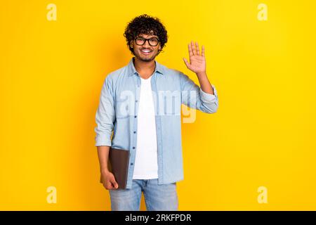 Portrait of cheerful guy it specialist hold netbook arm palm waving hi isolated on yellow color background Stock Photo