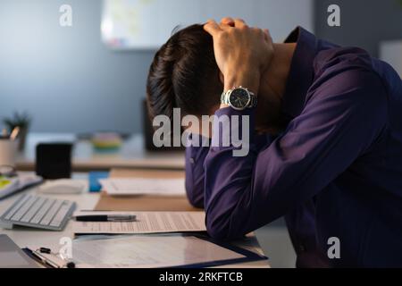 Stressed Accountant Sitting With Head In Hand While Working Late In Office Stock Photo