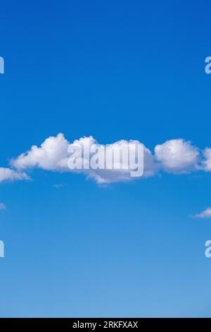 A vertical of a large white cumulus cloud in a deep blue sky on a sunny day Stock Photo
