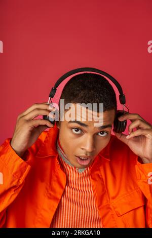stylish african american man listening music in wireless headphones on red background Stock Photo