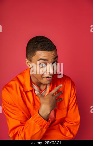 surprised african american man pointing with hand at himself and looking at camera on red Stock Photo