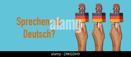 man hands holding microphones patterned with the german flag and the question do you speak german written in german in a panoramic format to use as we Stock Photo
