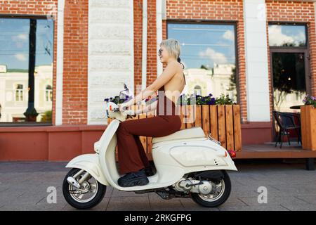 Young blond woman model riding on motorbike moped scooter in city street Stock Photo