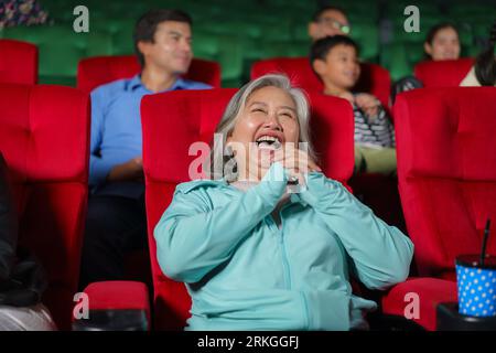 Asian elderly women are happy watching movies in the cinema, holding popcorn in their hands. Stock Photo