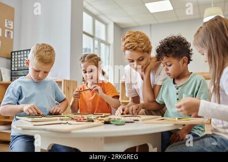 interracial children playing game near teacher in class in montessori school Stock Photo