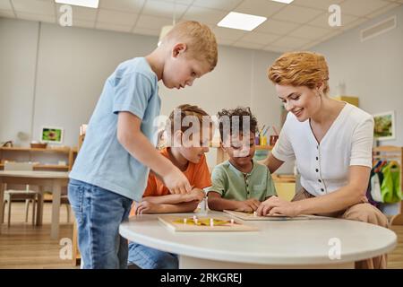 smiling teacher and interracial kids playing with didactic material in class in montessori school Stock Photo