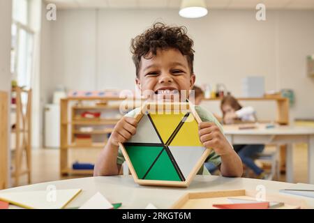 positive african american boy holding wooden didactic materials in blurred montessori school Stock Photo