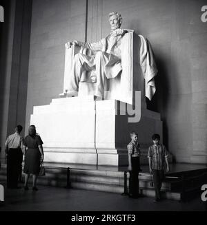 1960s, historical, visitors looking up at the large marble statue of Abraham Lincoln, inside the Lincoln Memorial in Washington DC, USA. The building is a temple for the memory of the 16th U.S President . Stock Photo