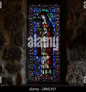 A vibrant stained glass window featuring a depiction of Saint John the Baptist set within a stone wall Stock Photo