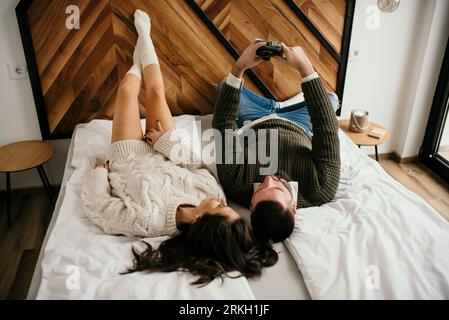 A young couple laying in bed, happily taking selfies with a camera smiling Stock Photo