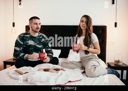 A young couple relaxing in bed drinking coffee and enjoying a moment together Stock Photo