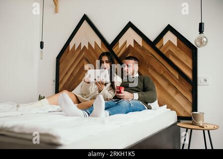 A young couple lounging in bed together, happily using a digital tablet in the comfort of their home Stock Photo