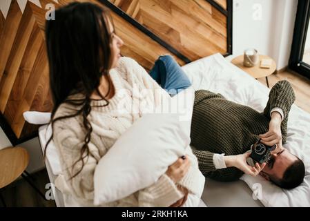 A young couple laying in bed, happily taking selfies with a camera smiling Stock Photo