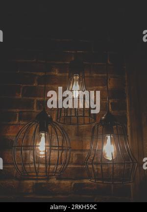 A closeup of three modern loft style lamps on a dark brick wall background Stock Photo