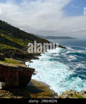 vertical landscape of a coastline with a person watching the sea from a giant rock, the waves hit the coast Stock Photo