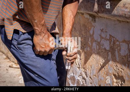 A male construction worker is using a hammer and nail to break through a concrete wall Stock Photo