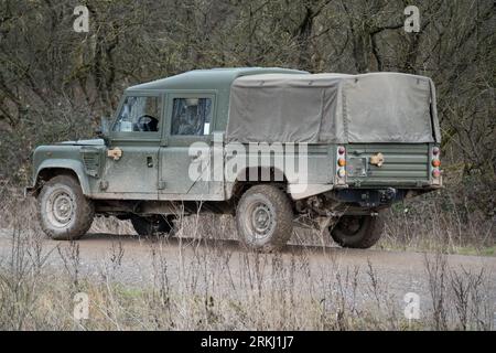 A medium size four-wheeled military utility vehicle is driving along a rugged mud track in Wilts, United Kingdom, during a military exercise Stock Photo