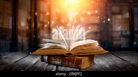 Old Book With Magic Lights And Bright Letters On Aged Table In Defocused Library Stock Photo