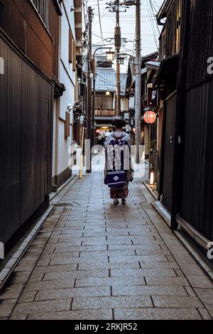 A sculpture of a young woman wearing a traditional Japanese kimono walks down a small Stock Photo