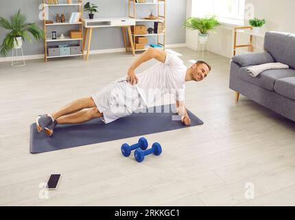 Happy, fit man having a fitness workout at home and doing a side plank exercise on a sports mat Stock Photo