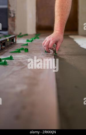 Close up hands of repairman laying tiles with tile leveling system on the floor in a new house. Stock Photo