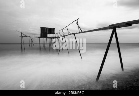 Black and white long exposure shot tulle effect near coastline with tiny wooden fisherman pier abstract photo Stock Photo