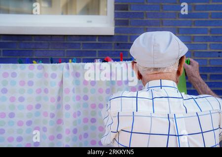Active elderly doing household. Unrecognizable retired man hanging up the laundry. Cooperation, responsibility and equality in domestic life Stock Photo
