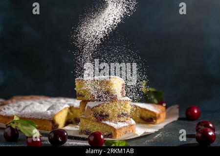 Powdered sugar decorates sponge cake with a cherry on a dark background. Homemade cooking Stock Photo