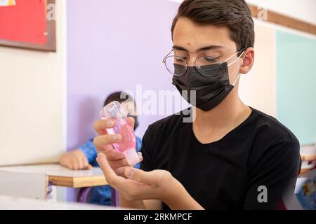 Teenager in school sterilizing his hands while wearing face mask to prevent infection Stock Photo