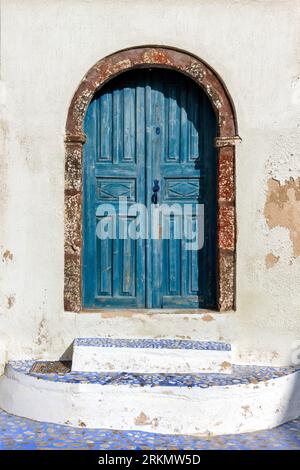 Traditional old wooden door of bluish-greenish color at an old house with ochre walls and stone threshold, in Pyrgos village of Santorini, Greece. Stock Photo