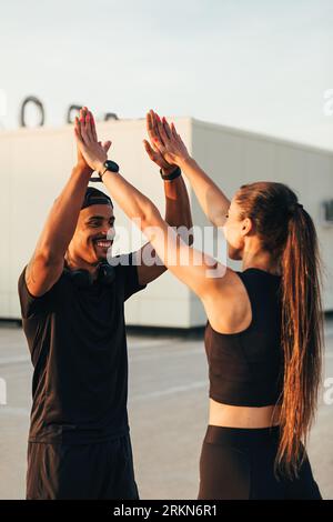 Two athletes in black sportswear giving high five on the roof Stock Photo