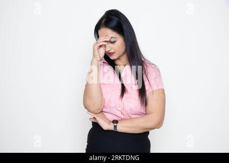 Stressed indian business woman wearing formal pink shirt standing isolated over white background. Workload and depression. Stock Photo